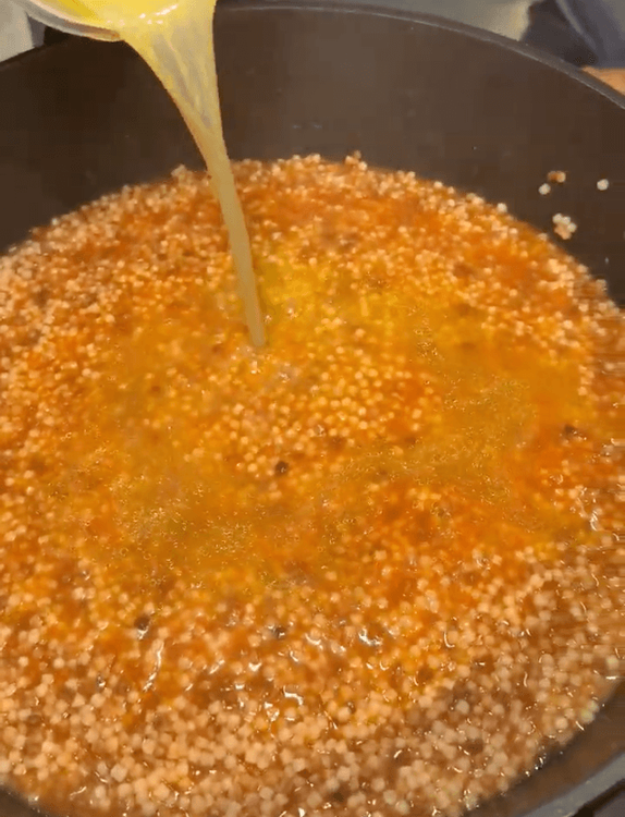cuisson de la fregola comme un risotto avec le versement du bouillon dans la poêle