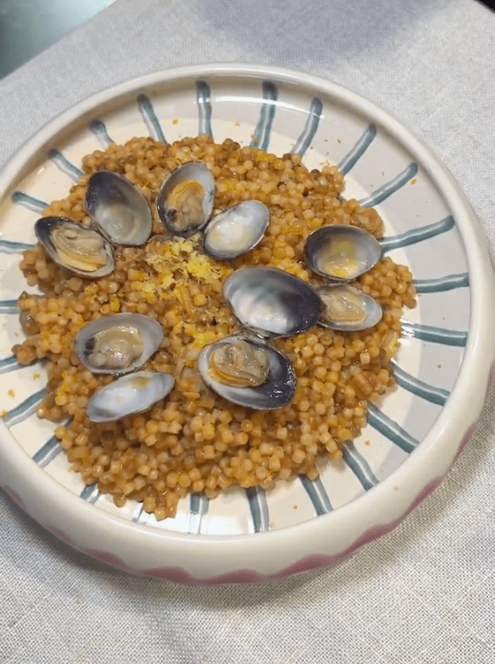 Assiette de fregola sarde aux palourdes dressée avec des palourdes en décoration