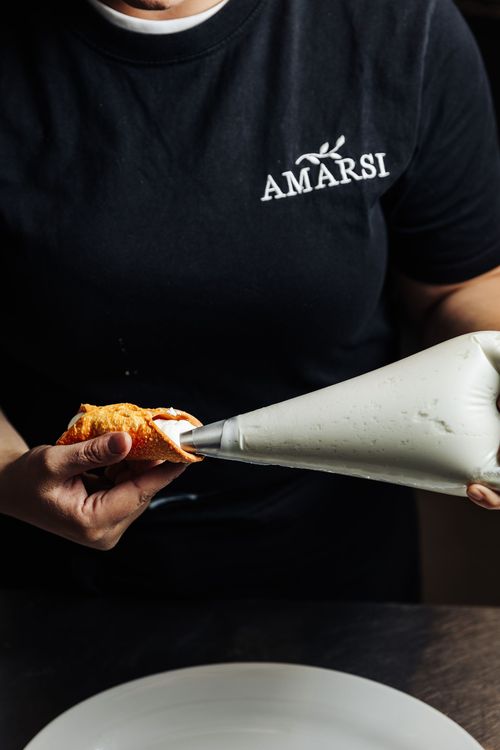la cheffe de cuisine rempli un cannoli de ricotta sucrée avec une poche à douille
