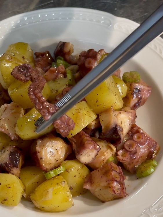 dressage à la pince d'une salade de pomme de terre, poulpe, céleri et oignon dans une assiette blanche